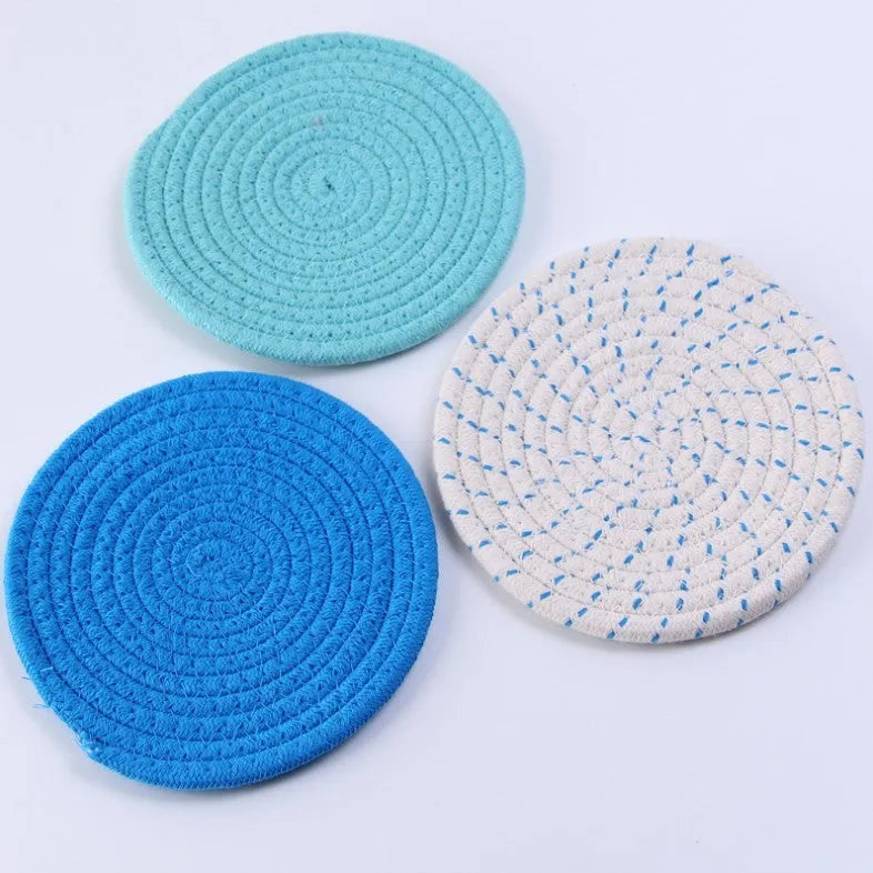 Set of three round grey cotton cord coasters on a wooden table.