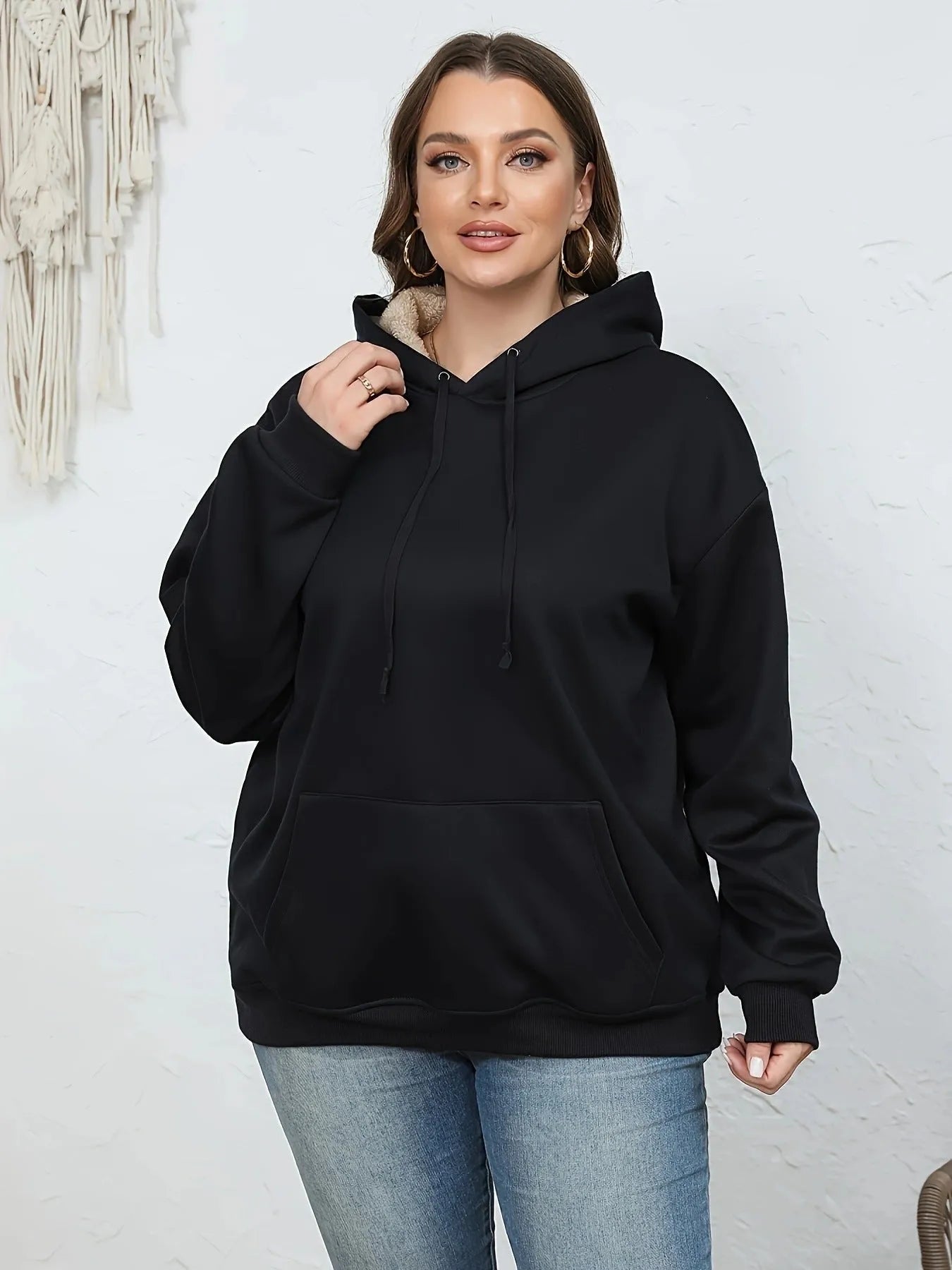 A woman wearing a thick, grey, loose-fit hooded sweatshirt with a 3D pattern and front pockets.