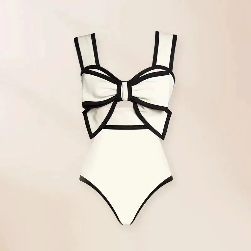 A black one-piece swimsuit for women with a white detachable skirt and a decorative bow at the front.