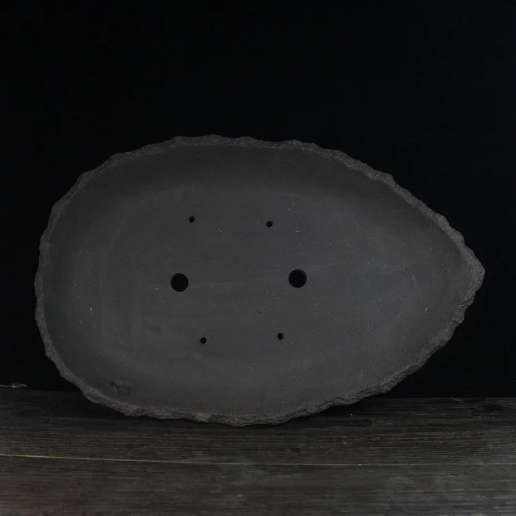 Handmade purple clay flowerpot in a unique shape, shown on floor beside a plant.