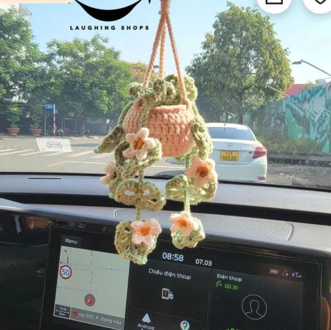 Green and white knitted wool car plant decoration with macramé texture and a white hanging rope.