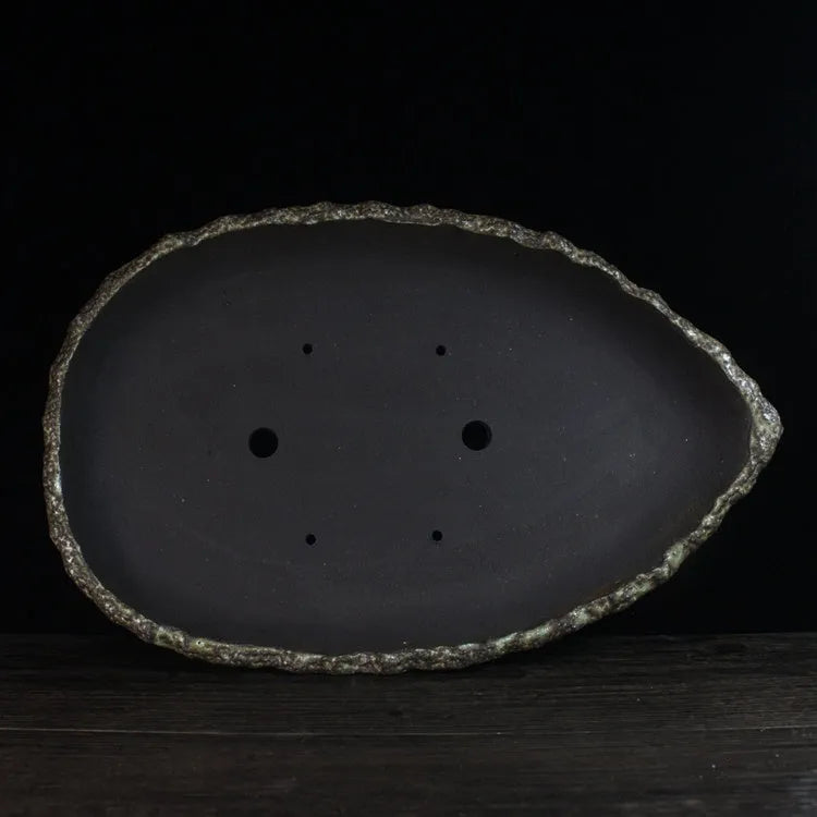 Handmade purple clay flowerpot in a unique shape, shown on floor beside a plant.
