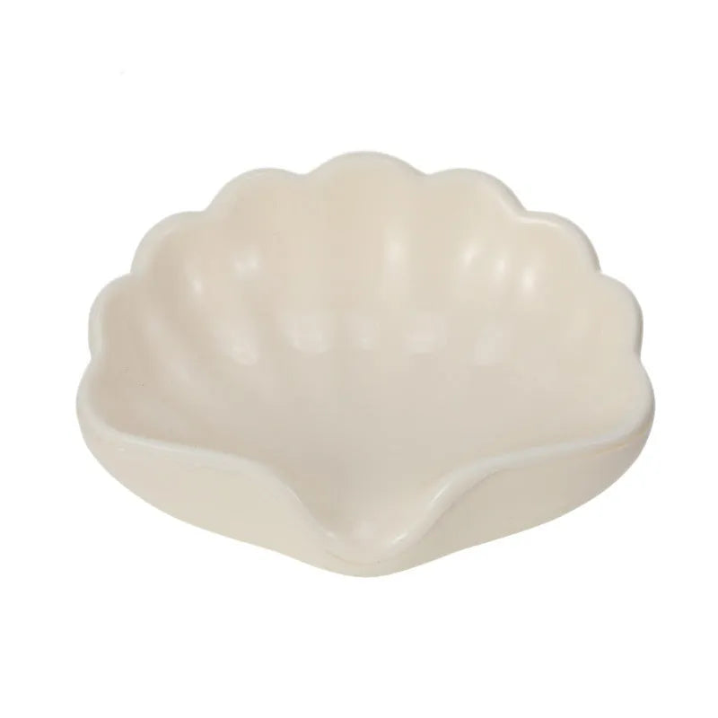White or pink plastic shell-shaped soap dish with slatted base for bathroom use.