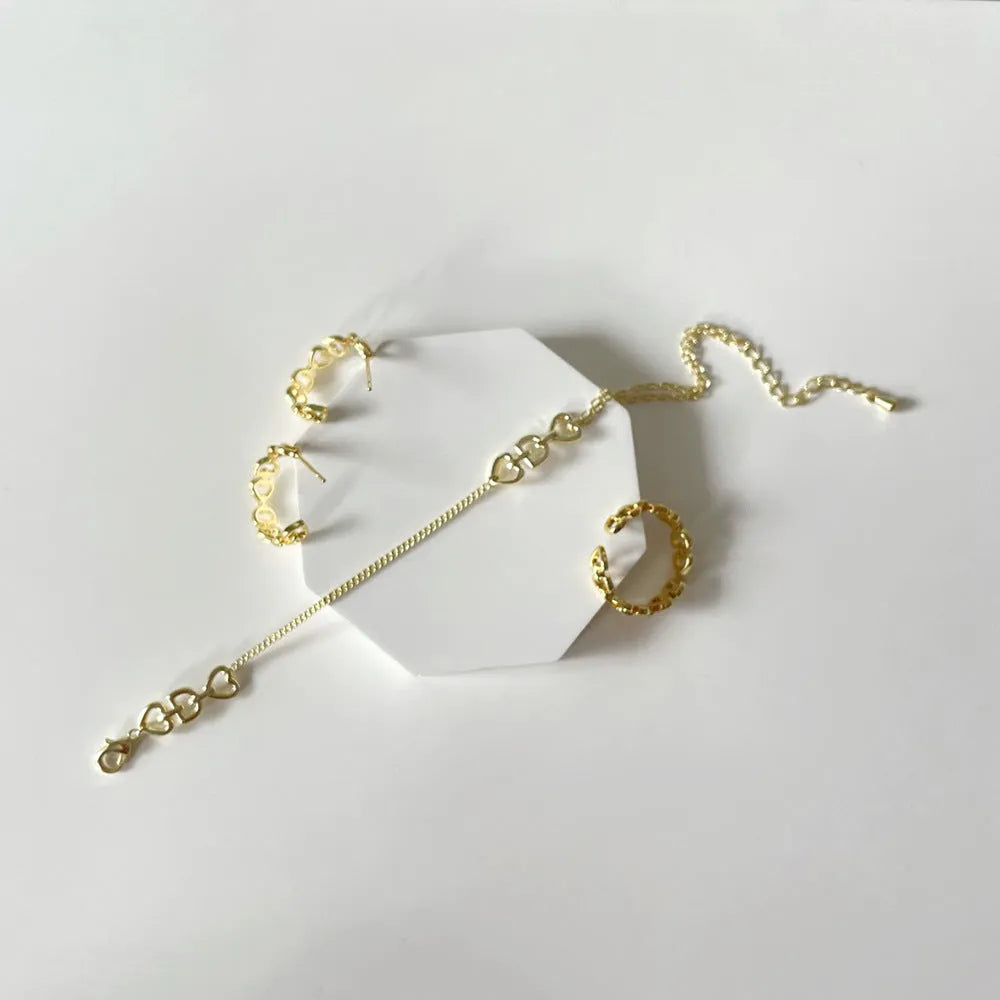 Minimalist Love Letter D geometric jewellery set including gold-plated earrings, ring, and bracelet on a light background