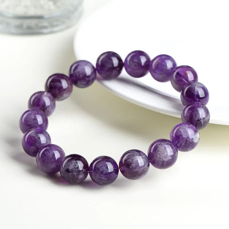 Natural feather amethyst crystal bracelet with scattered purple beads on a white background.