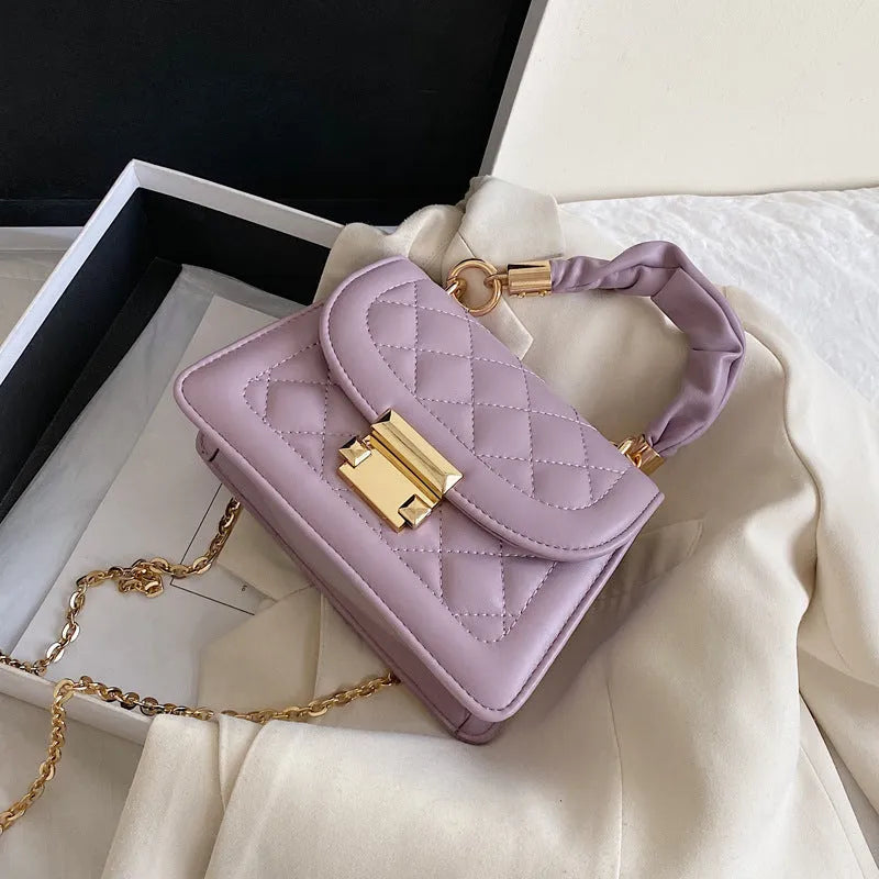 Small square purple shoulder bag with rhombus pattern showing crossbody strap and interior compartment.