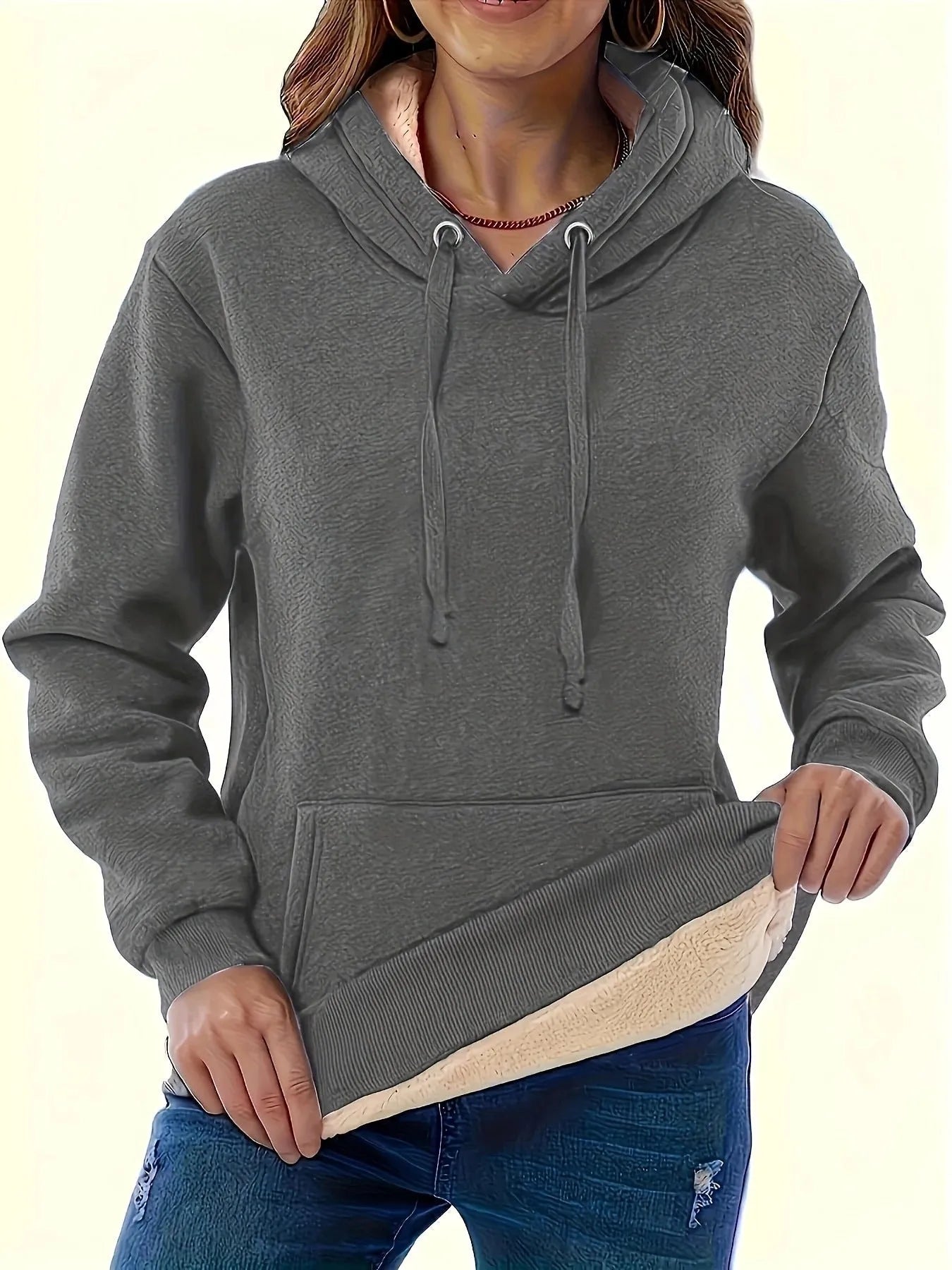 A woman wearing a thick, grey, loose-fit hooded sweatshirt with a 3D pattern and front pockets.