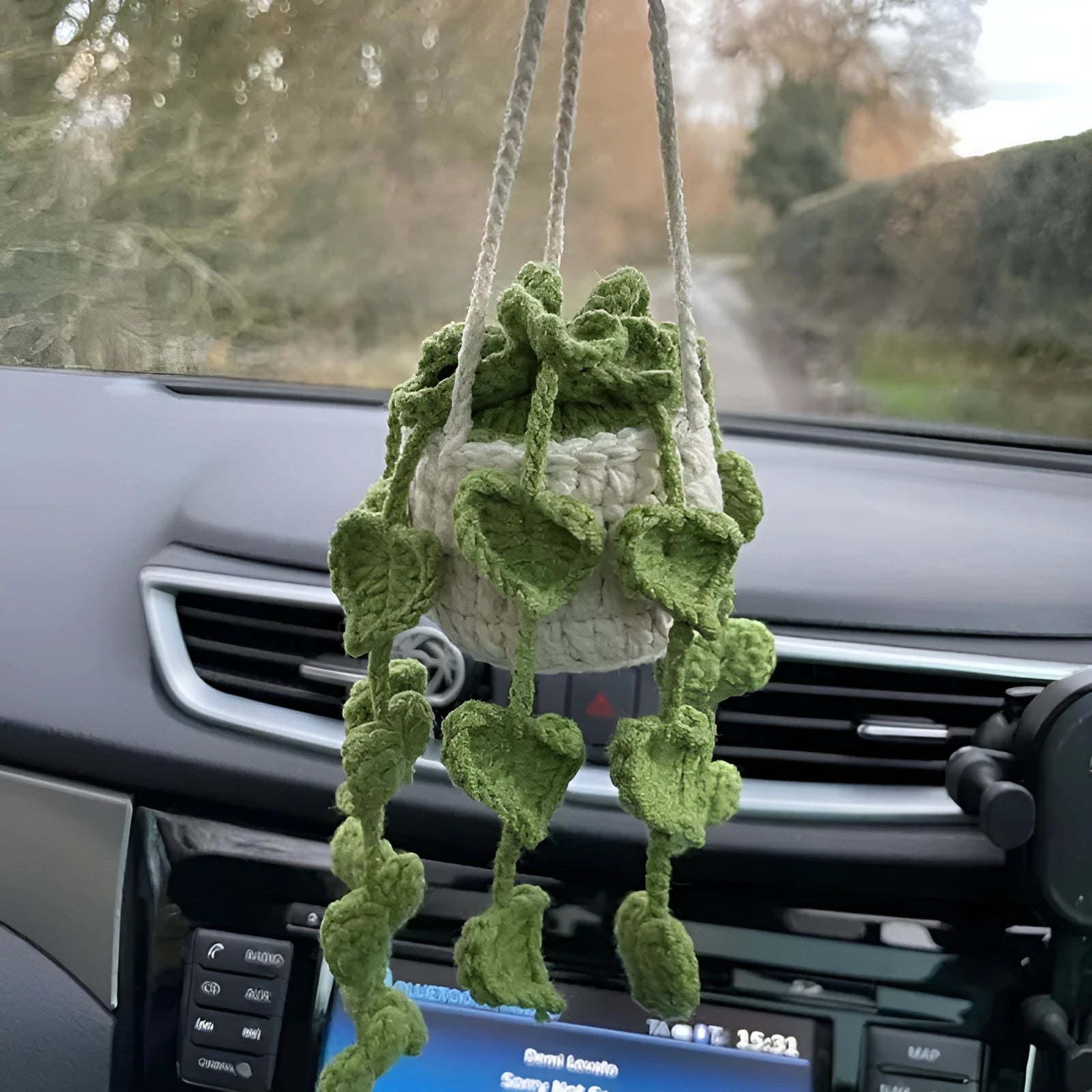 Green and white knitted wool car plant decoration with macramé texture and a white hanging rope.