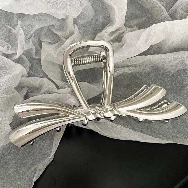 Assorted silver metal hair claws and barrettes including wave, knot, bow, and pearl designs on a white background.