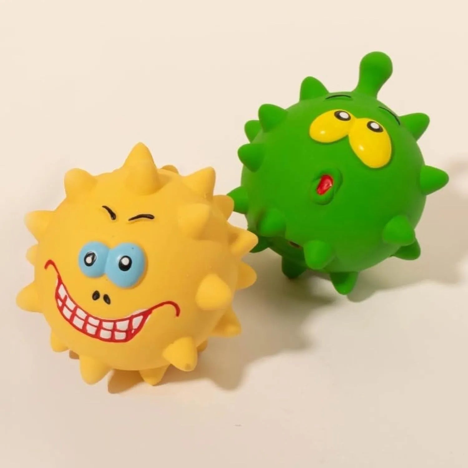 Set of four coloured latex squeaky dog balls with cute faces on a bumpy surface.