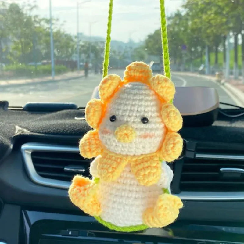 Green and white knitted wool car plant decoration with macramé texture and a white hanging rope.