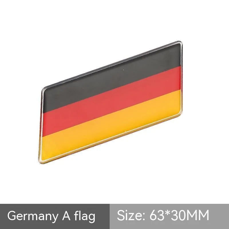 Aluminium parallelogram car sticker showing a national flag design, measuring 6.3 by 3 centimetres.