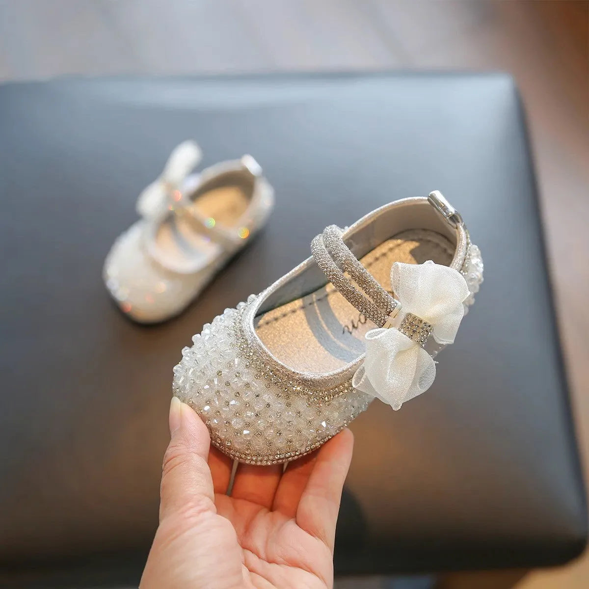 Silver soft bottom synthetic leather baby pumps with low top, bow detail, and Velcro fastening
