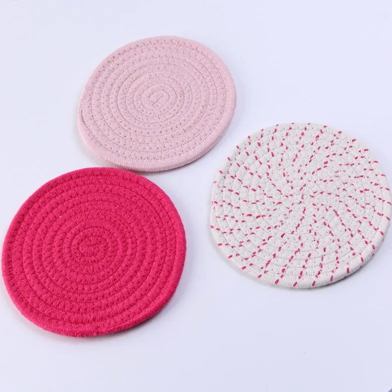 Set of three round grey cotton cord coasters on a wooden table.