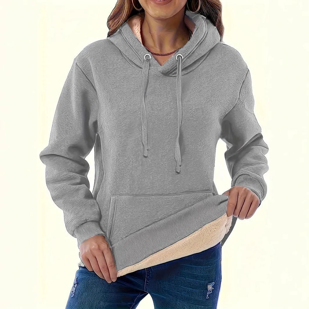 A woman wearing a thick, grey, loose-fit hooded sweatshirt with a 3D pattern and front pockets.