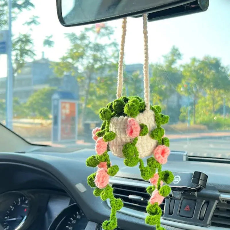 Green and white knitted wool car plant decoration with macramé texture and a white hanging rope.