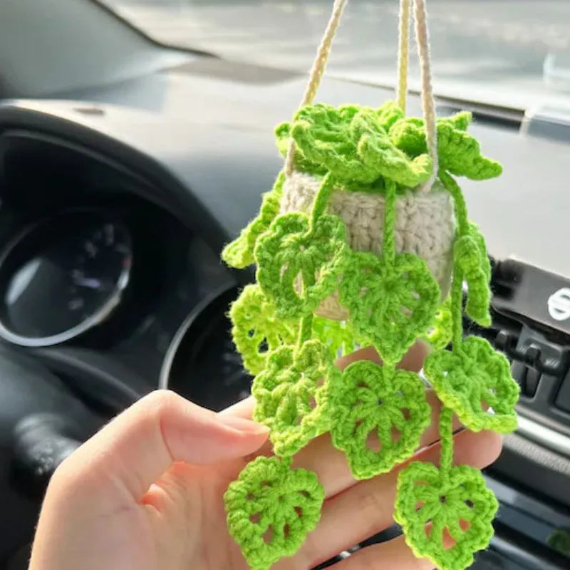Green and white knitted wool car plant decoration with macramé texture and a white hanging rope.