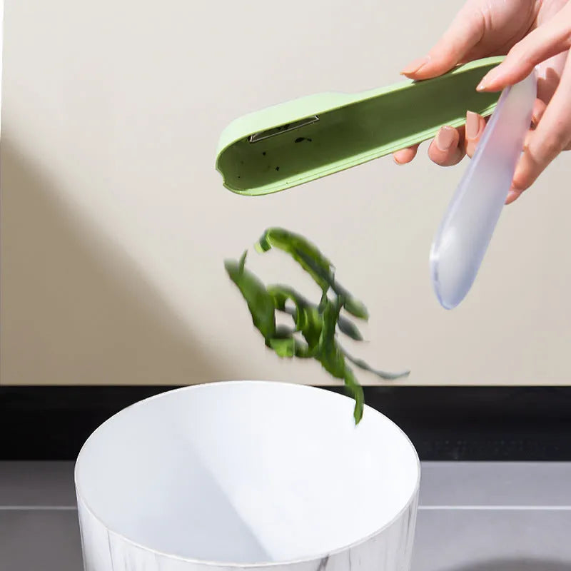 Green vegetable peeler with storage tube, non-slip handle, and hang hole on a kitchen worktop.