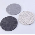 Set of three round grey cotton cord coasters on a wooden table.