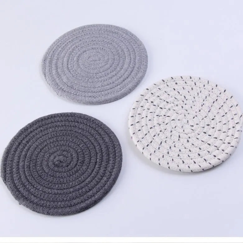 Set of three round grey cotton cord coasters on a wooden table.