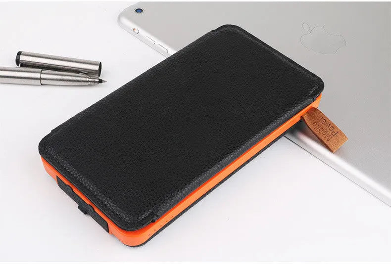 Black solar power bank with a solar panel, showing its USB ports and LED light, placed outdoors on a rock.