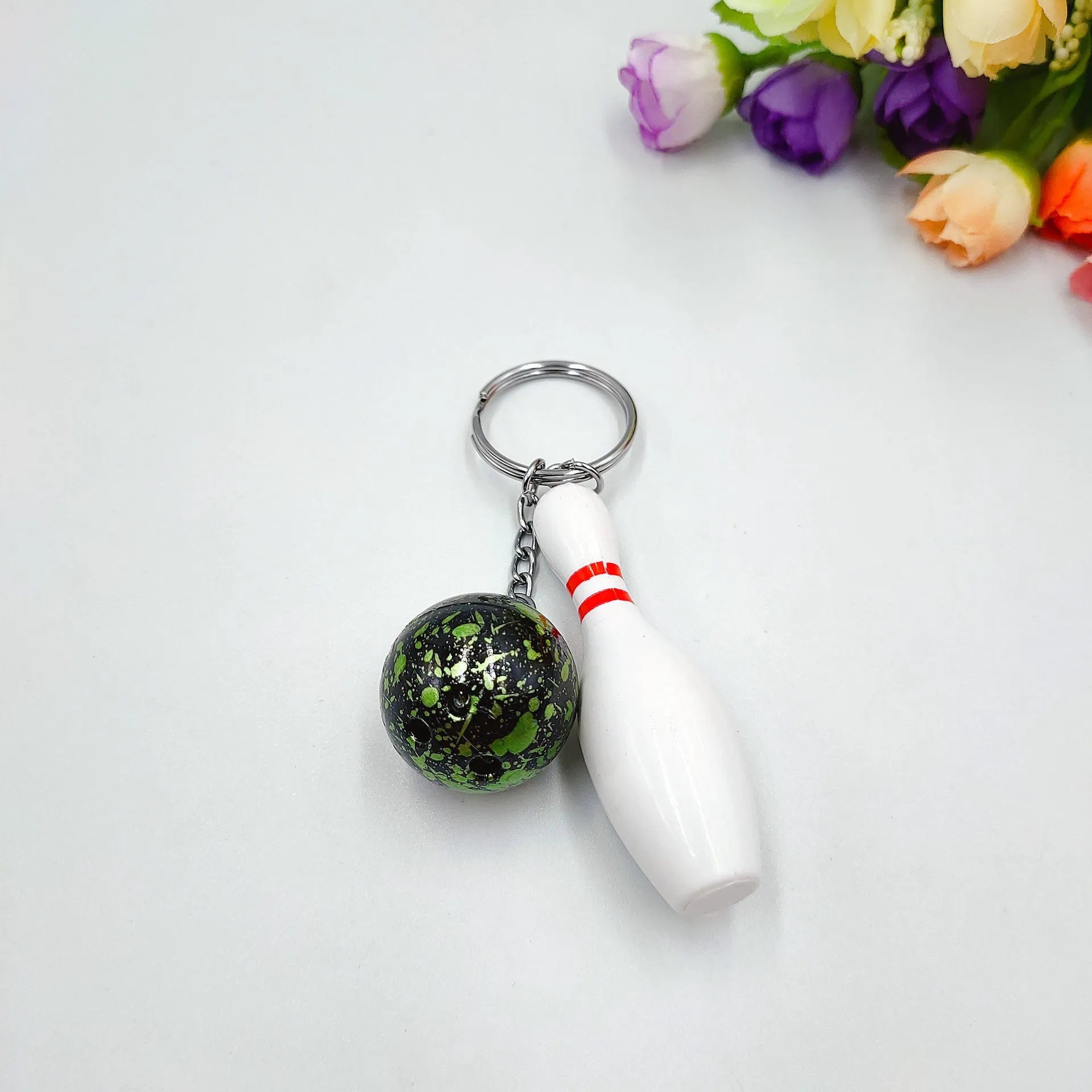 Miniature dark red bowling ball keychain on a metal key ring against a white background.