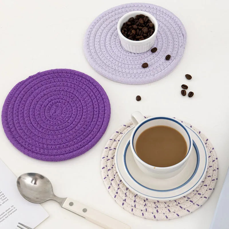 Set of three round grey cotton cord coasters on a wooden table.