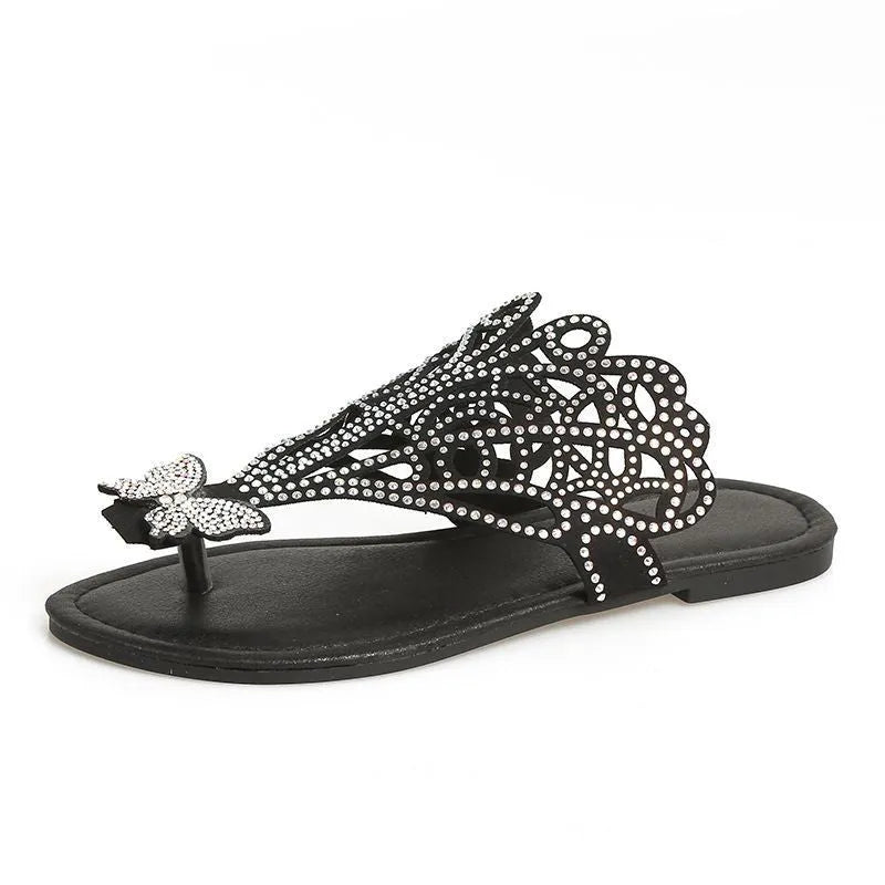 Women's black slip-on sandals with rhinestone accents and a hollow-out design on a flat rubber sole.
