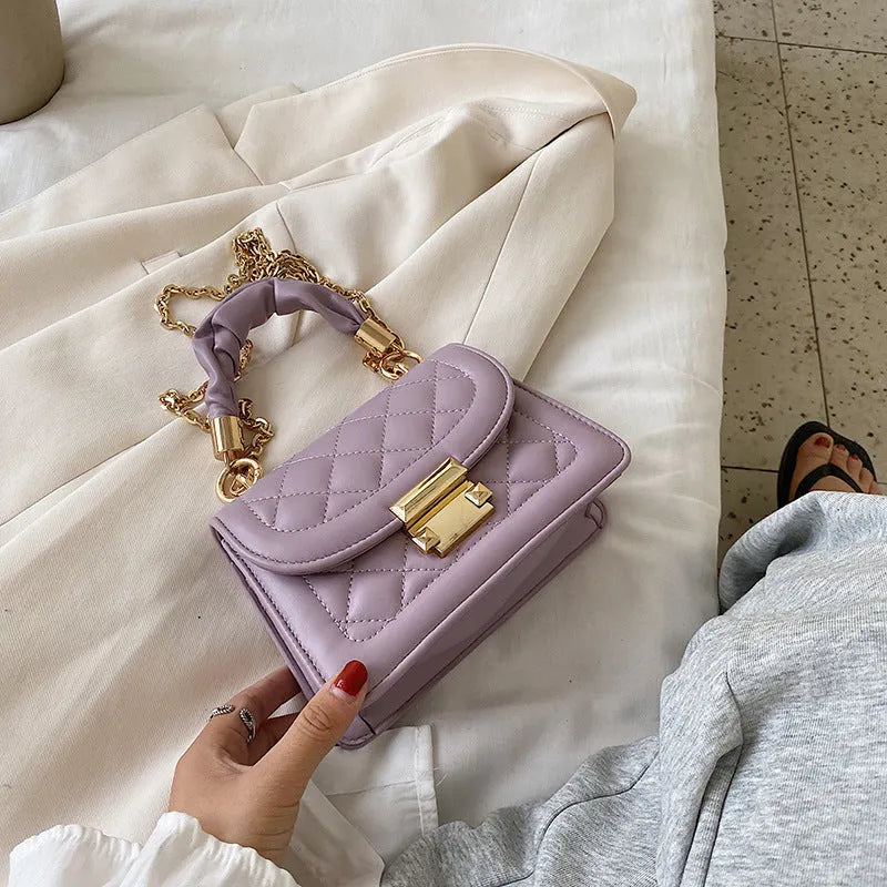 Small square purple shoulder bag with rhombus pattern showing crossbody strap and interior compartment.
