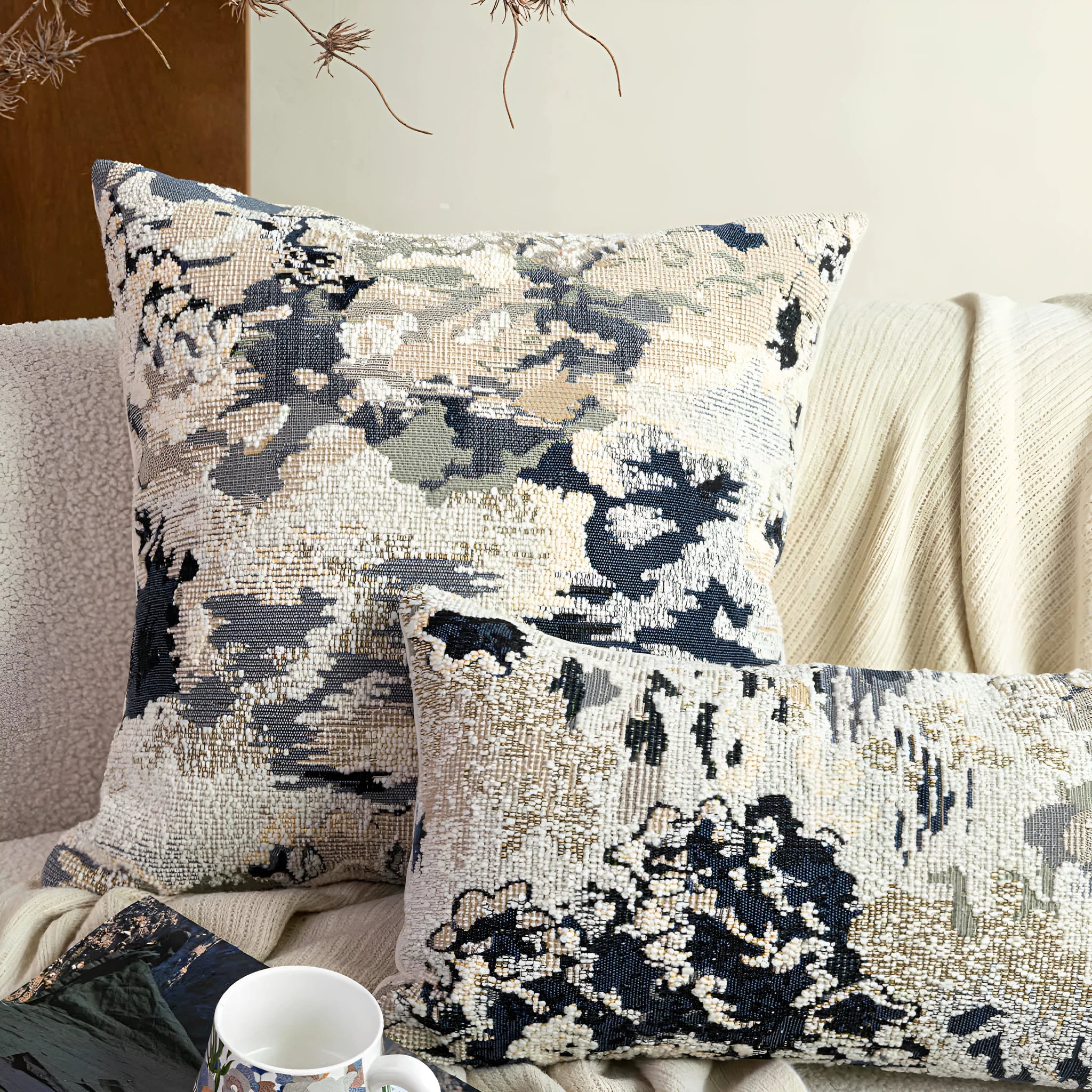 Blue decorative pillow with abstract flower pattern in 50x50cm square size on a grey sofa.