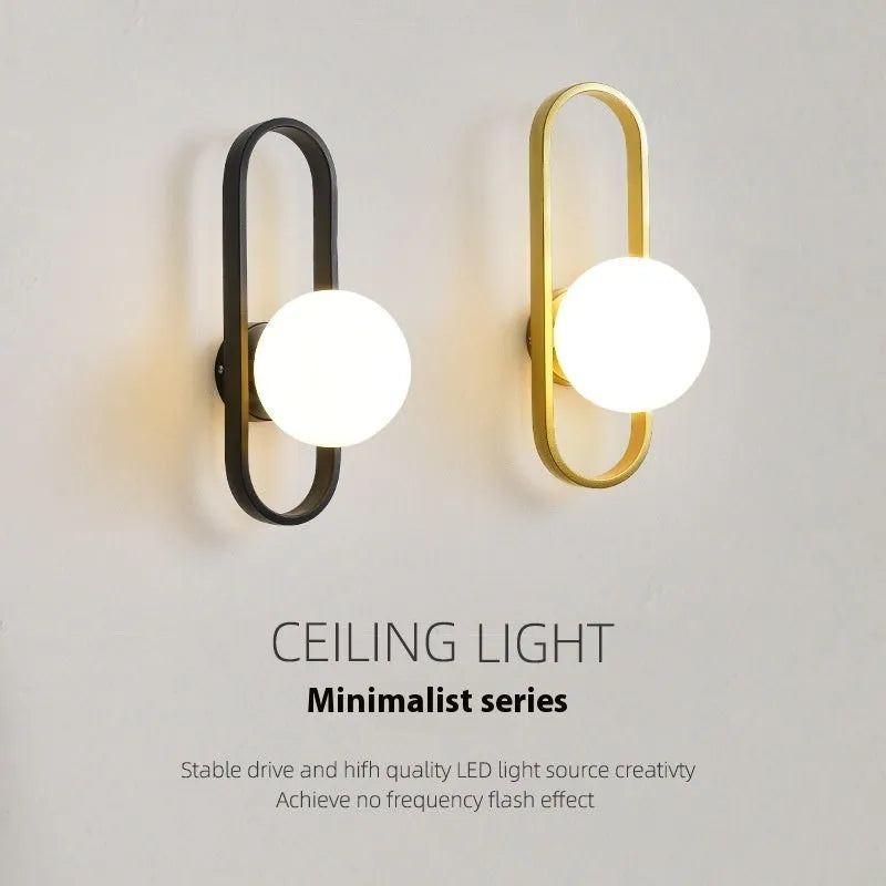 Minimalist modern wall lamp with a clear glass shade on an iron body, shown in a black finish mounted on a wall.