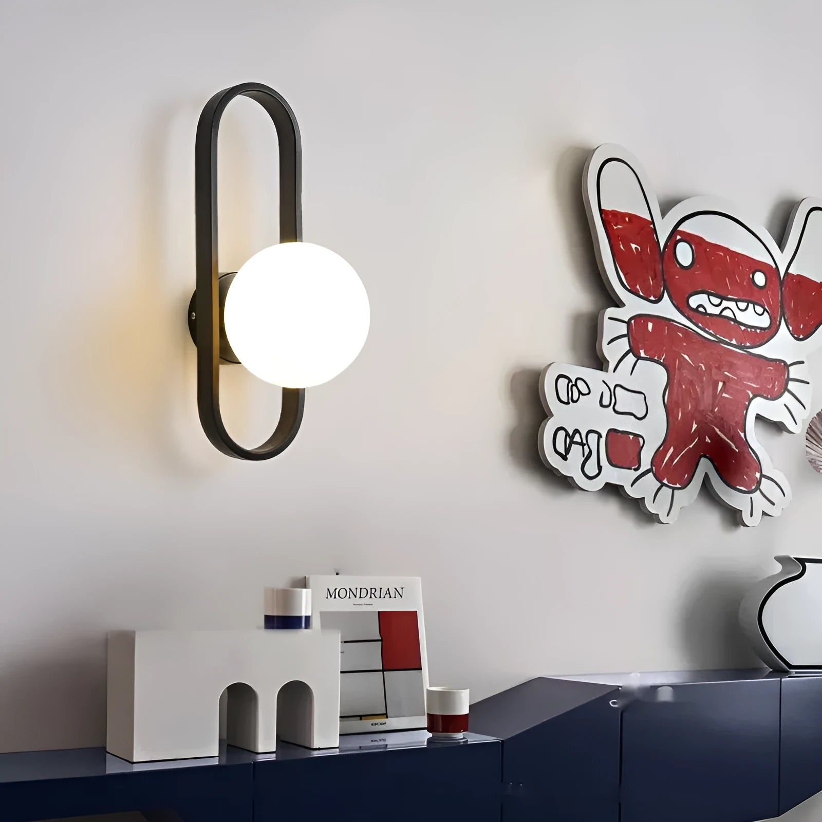 Minimalist modern wall lamp with a clear glass shade on an iron body, shown in a black finish mounted on a wall.