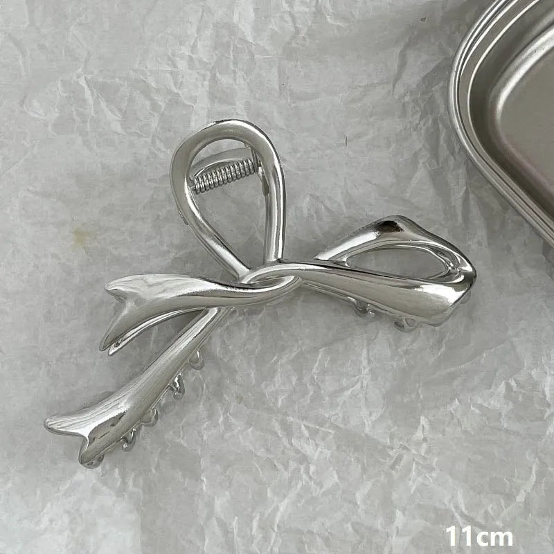 Assorted silver metal hair claws and barrettes including wave, knot, bow, and pearl designs on a white background.
