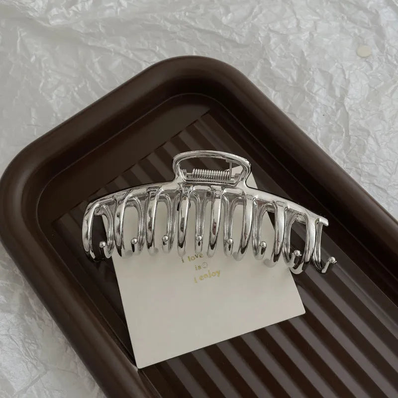 Assorted silver metal hair claws and barrettes including wave, knot, bow, and pearl designs on a white background.