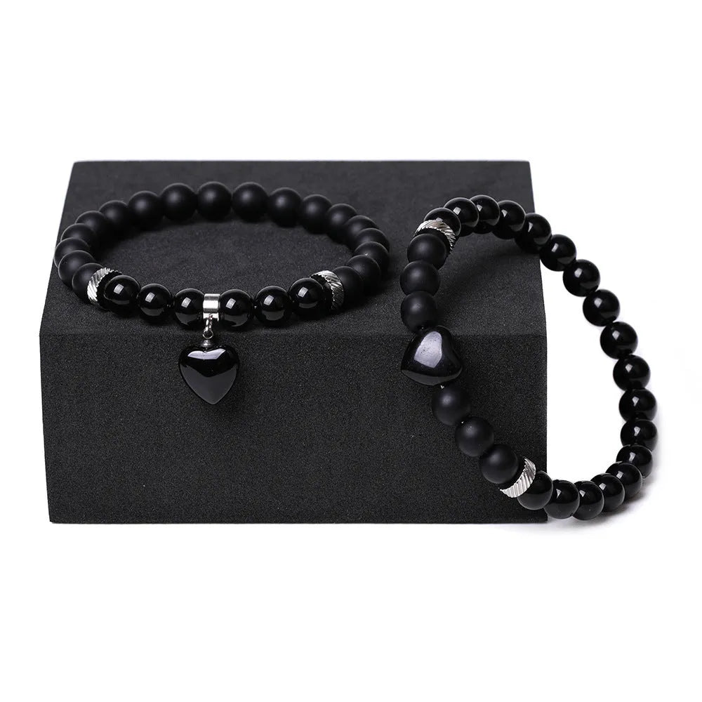 A pair of matching bracelets with polished geometric heart pendants made from natural stone.