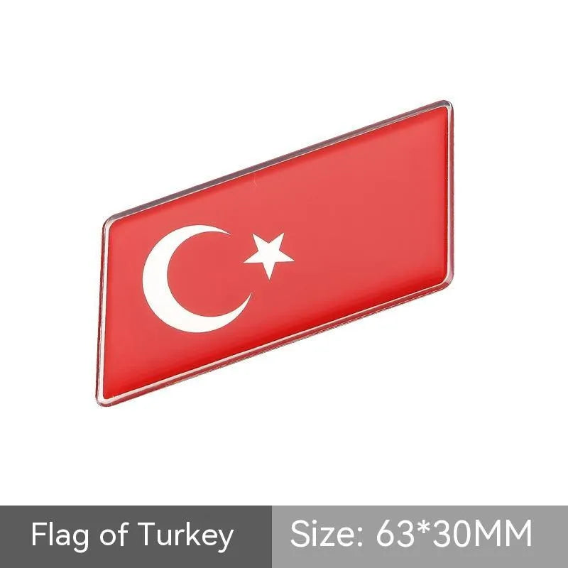 Aluminium parallelogram car sticker showing a national flag design, measuring 6.3 by 3 centimetres.