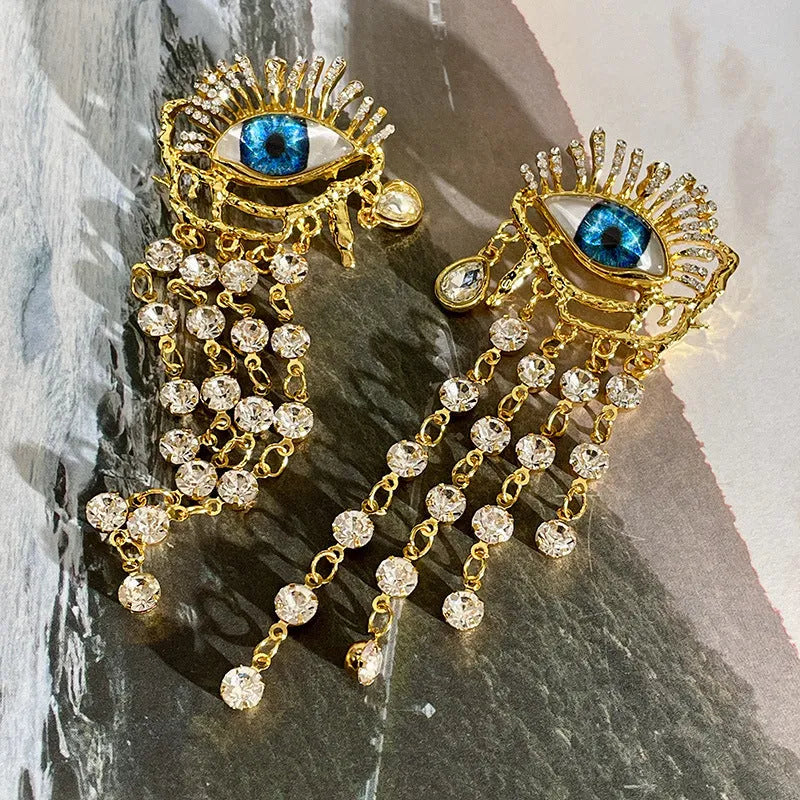 Pair of gold plated long tassel earrings with artificial crystal and zircon elements, eye motif, on white background