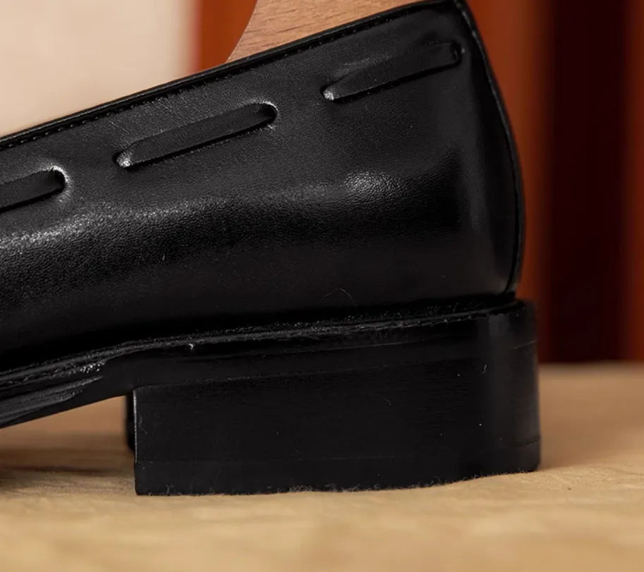 Men's black leather slip-on loafers with fringe detailing on a wooden floor