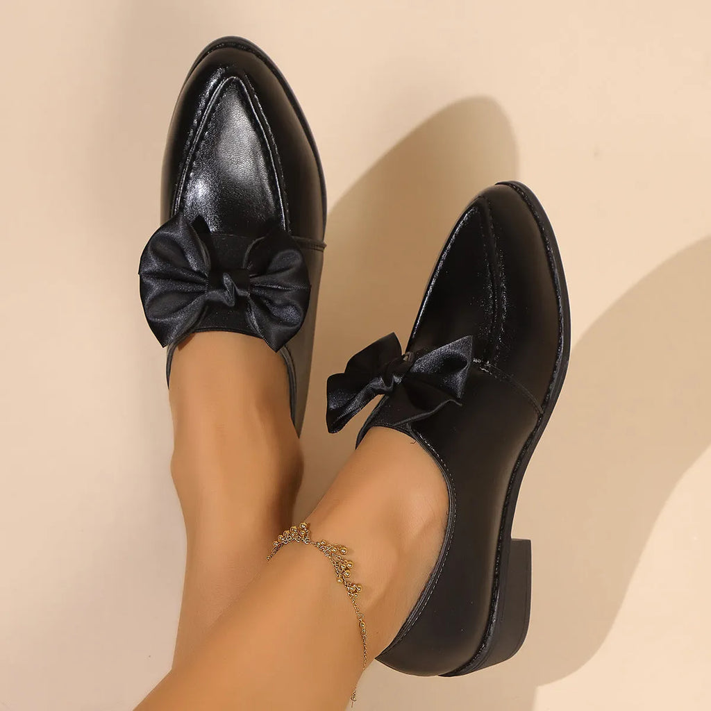 Women's beige loafers with a large decorative bow, showcasing rounded toe and slip-on design.