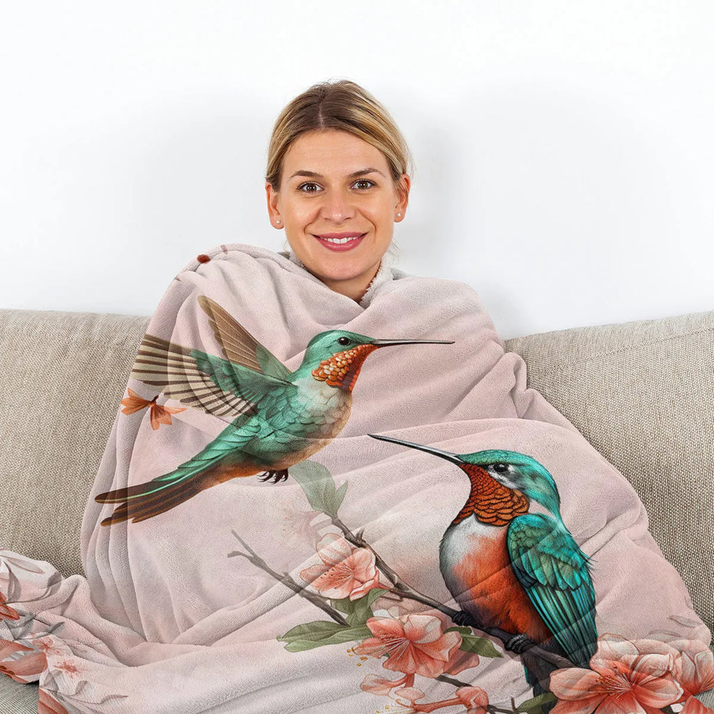 Hummingbird floral fleece throw blanket in pink flannel velvet, shown on sofa with hemmed edges
