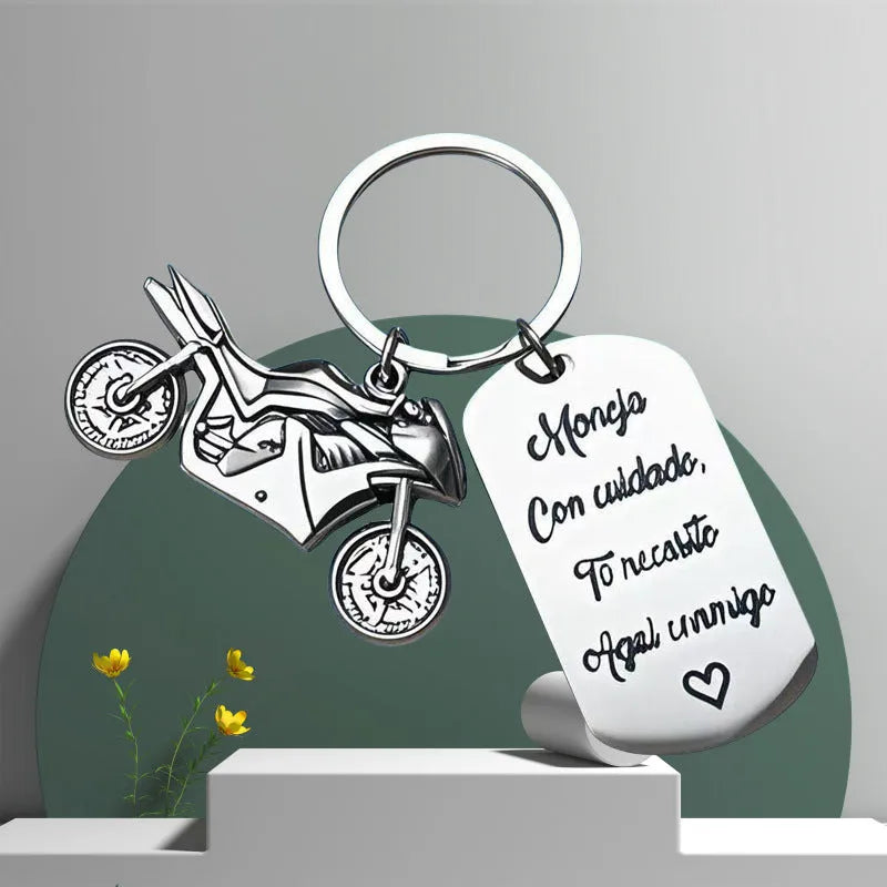 Stainless steel key ring with etched motorcycle design next to a grey flannel drawstring bag.