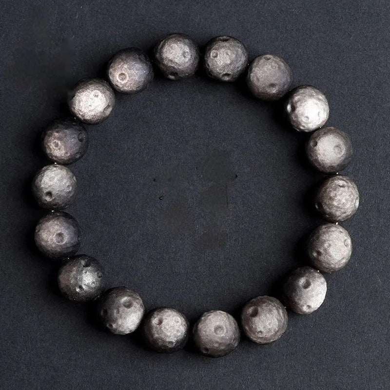 Natural obsidian crater ball bracelet with meteorite-like texture in silver stone or gold finish.