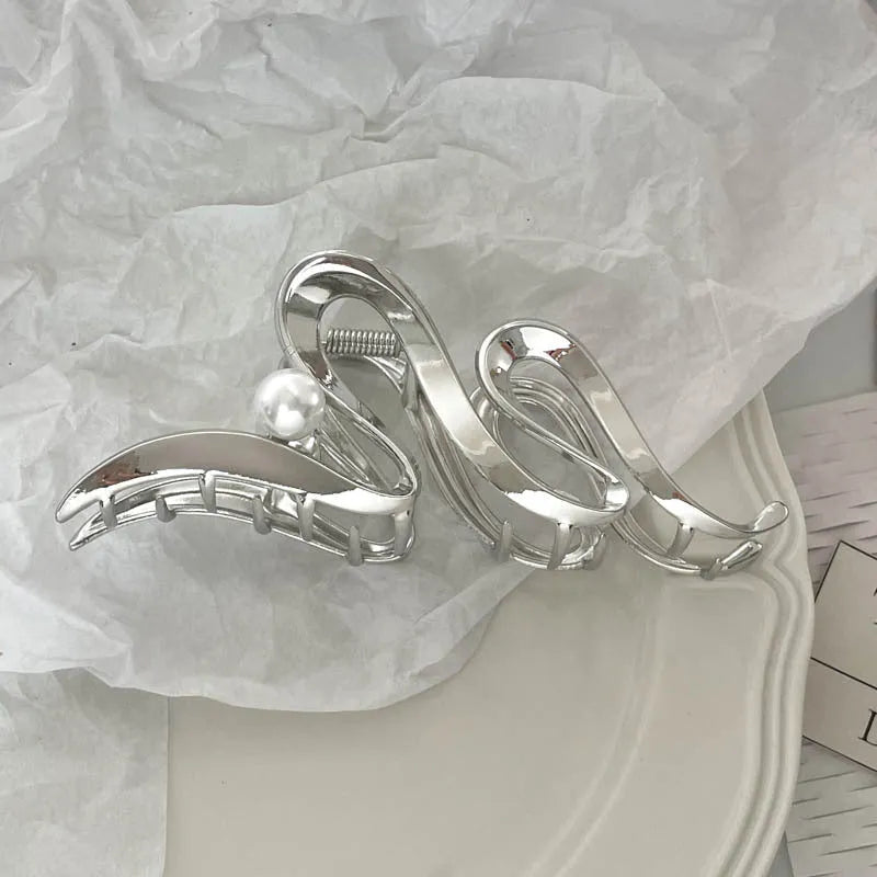 Assorted silver metal hair claws and barrettes including wave, knot, bow, and pearl designs on a white background.