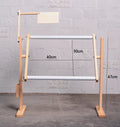 Vertical adjustable solid wood cross stitch embroidery frame in natural log colour on a desktop.