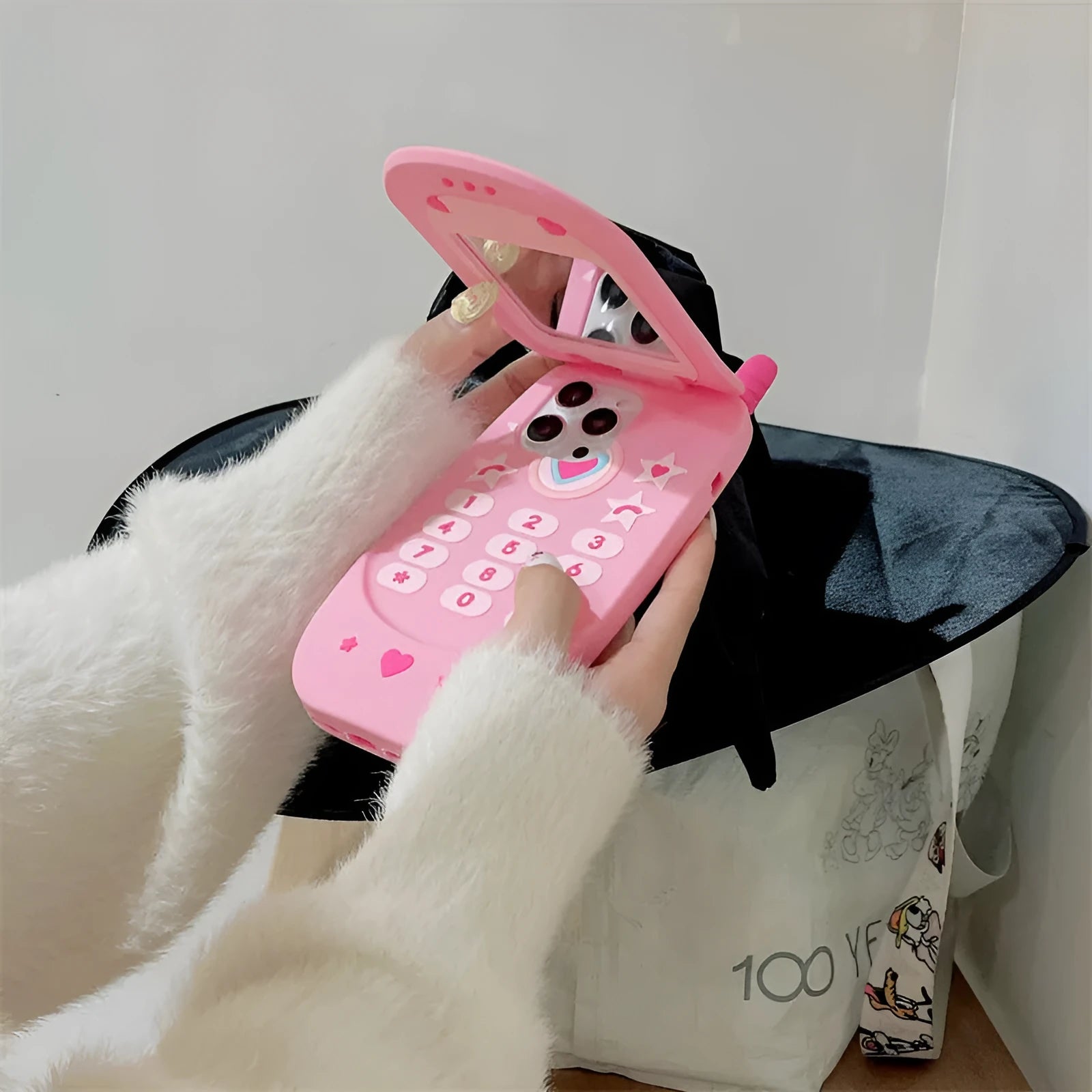 Pink silicone iPhone case shaped like a flip phone with a built-in mirror, showing cute cartoon style.