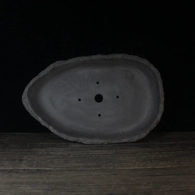 Handmade purple clay flowerpot in a unique shape, shown on floor beside a plant.