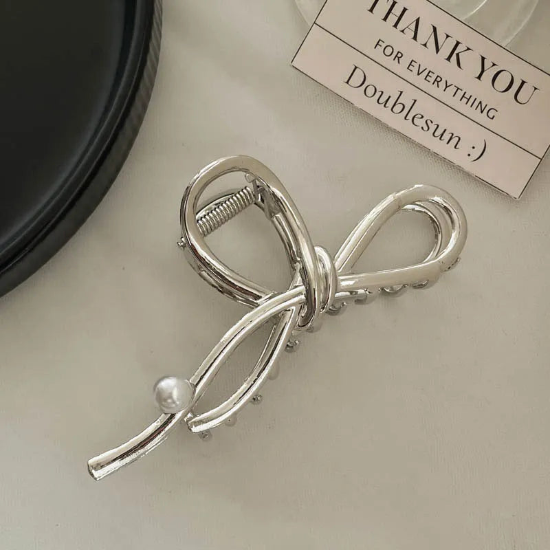 Assorted silver metal hair claws and barrettes including wave, knot, bow, and pearl designs on a white background.