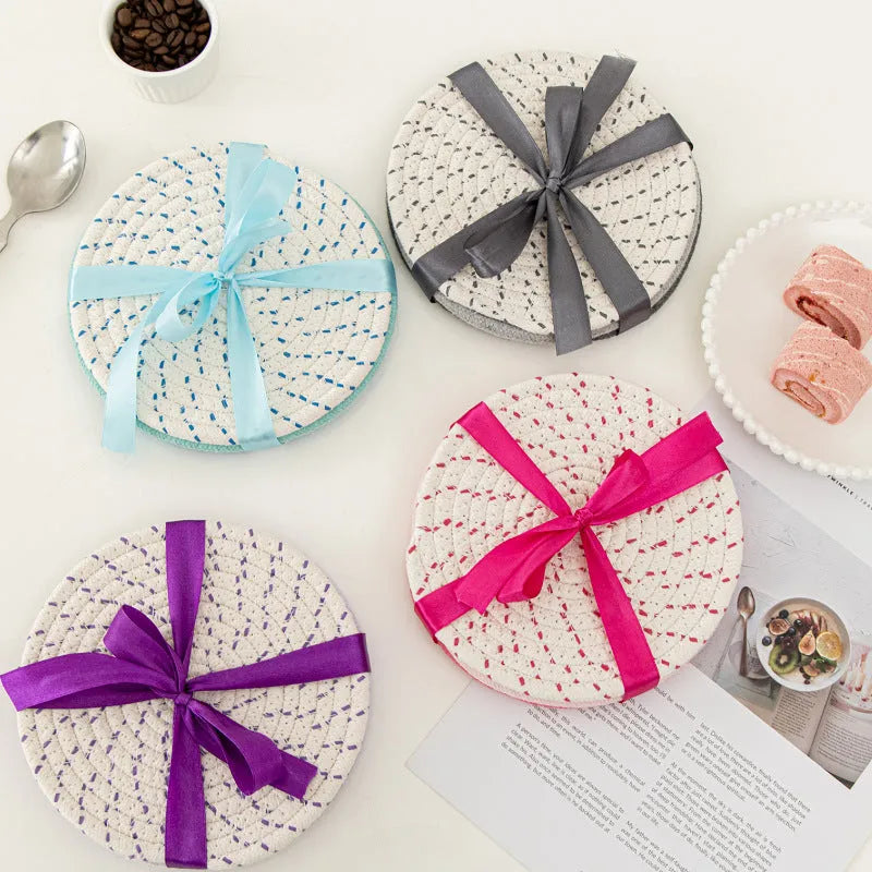 Set of three round grey cotton cord coasters on a wooden table.