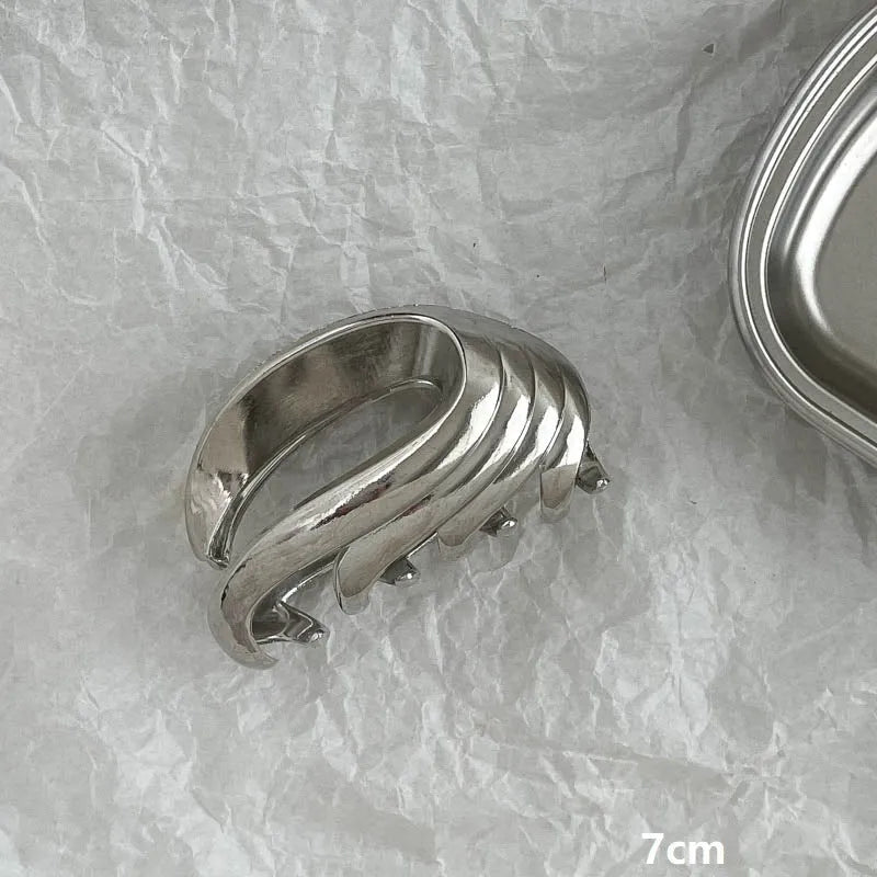 Assorted silver metal hair claws and barrettes including wave, knot, bow, and pearl designs on a white background.