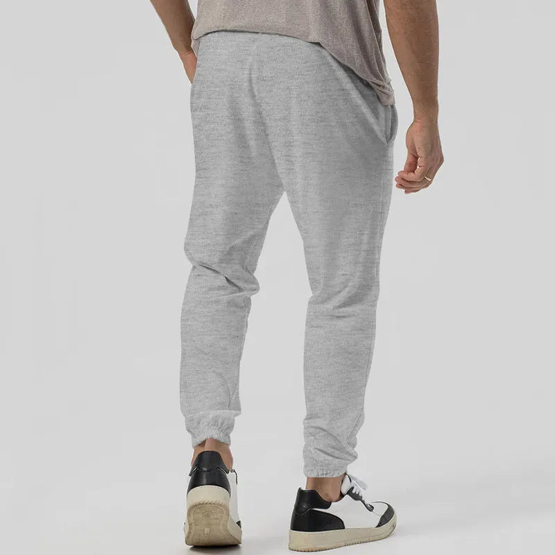 Man wearing gray straight-leg casual track sweatpants with a tapered fit and elastic waistband.